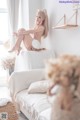 A woman sitting on top of a white couch next to a window.