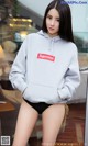 A woman wearing a grey hoodie with a red Supreme box logo on it.