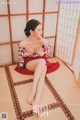 A woman in a red and white kimono sitting on a tatami mat.