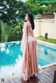 A woman in a pink dress standing by a swimming pool.