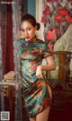 A woman in a green and orange cheongsam posing for a picture.