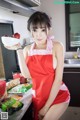 A woman in a red apron holding a bowl of fruit.