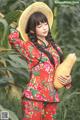 A woman in a red dress and straw hat holding a squash.