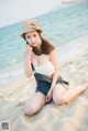 A woman sitting on the beach wearing a hat.