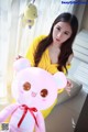 A woman in a yellow dress holding a pink teddy bear.