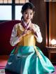 A woman in a blue and yellow hanbok sitting on a red couch.